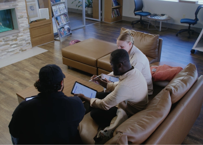Students sitting on a modern couch reviewing their school notes on their iPads